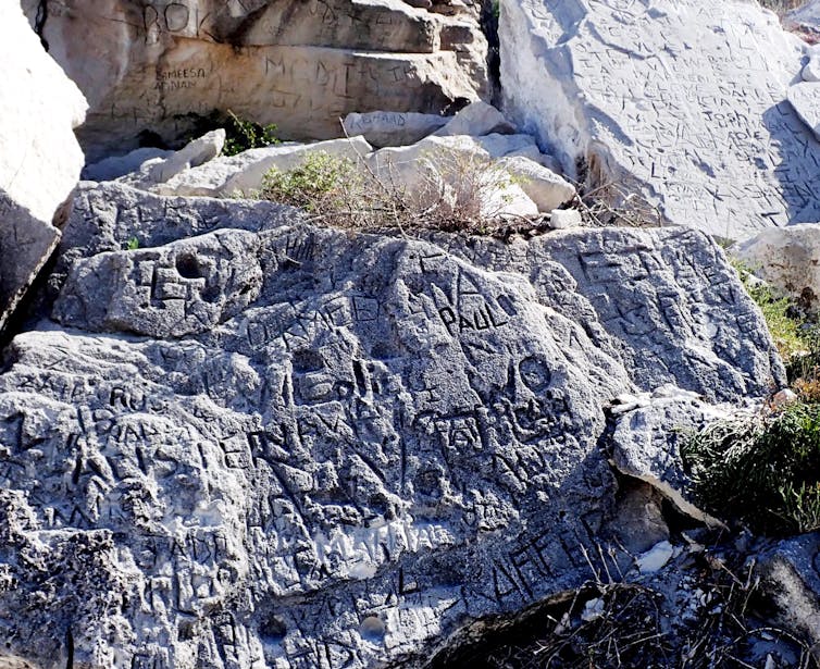 A large grey rock-like surface is covered in deeply etched names and words