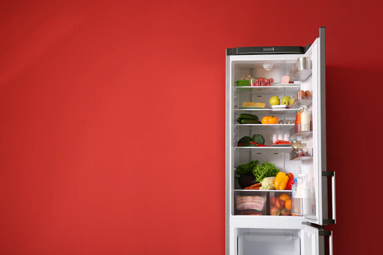 An open fridge full of fresh food against a red wall