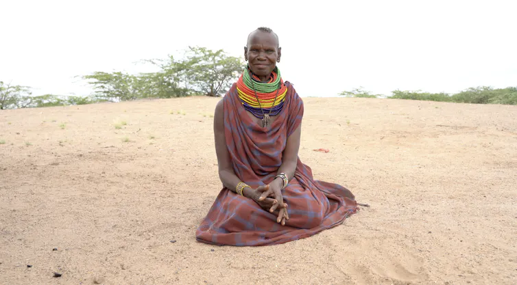 A woman sits on sand, smiling at the camera.