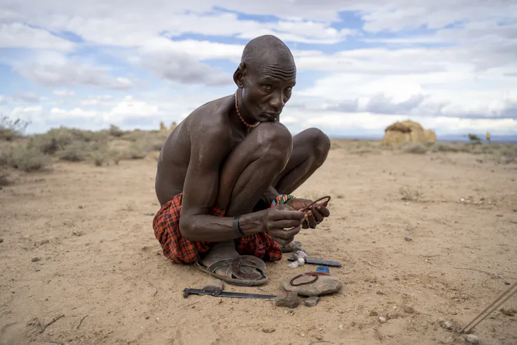 A man crouches on the sand amongst some tools