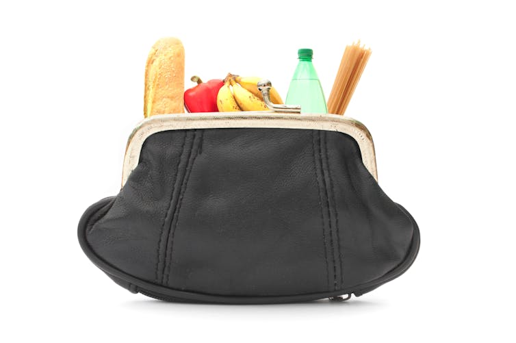 Large purse filled with various groceries including fruit and bread.