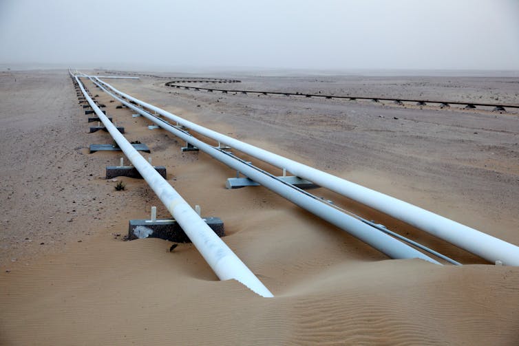 White gas pipes pass beneath sand in a desert.