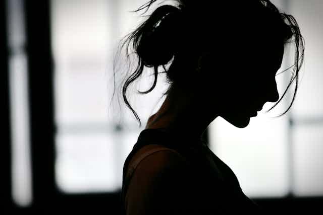 A woman is silhouetted against a window.