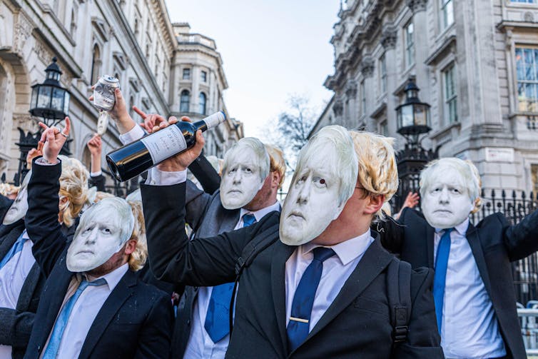 Protestors wearing Boris Johnson masks waving bottles of wine outside Downing Street
