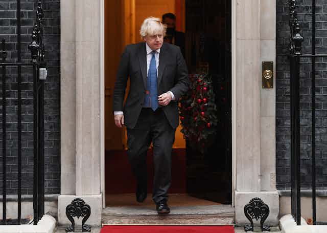 Boris Johnson walking out of Number 10 Downing Street which has a Christmas wreath on the door