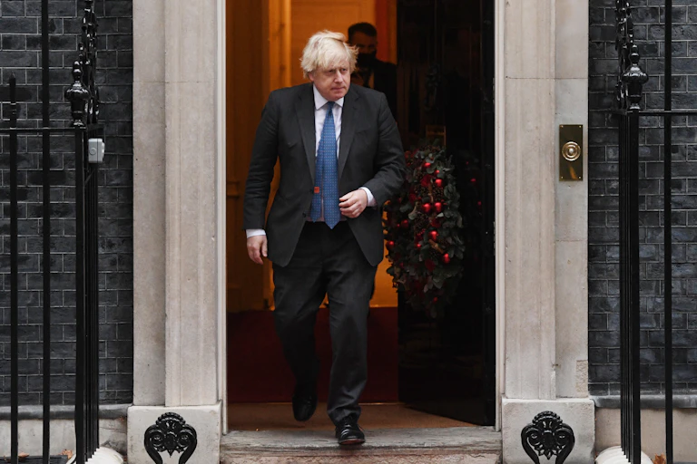 Boris Johnson walking out of Number 10 Downing Street which has a Christmas wreath on the door