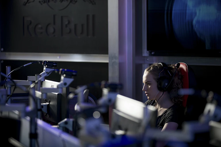 a woman wearing headphones looks at one of a row of computer monitors in a darkened room