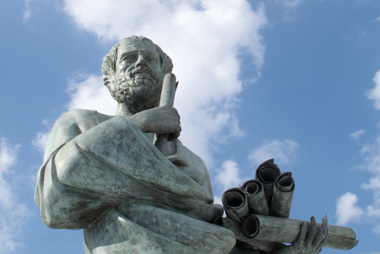 A statue of Greek philosopher Aristotle holding rolled sheaves of paper.
