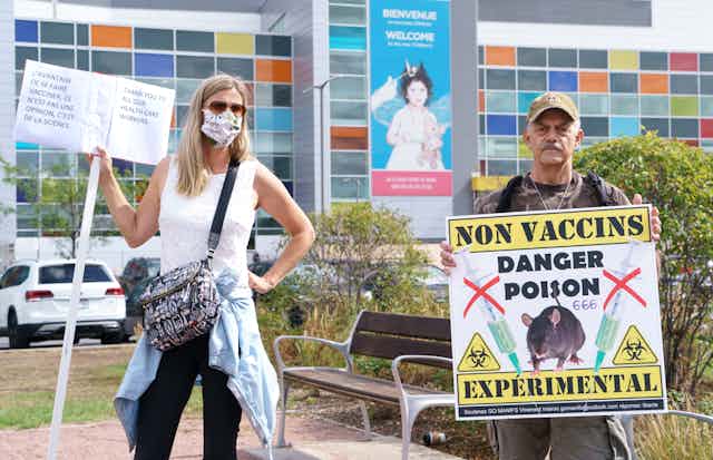 Une femme et un homme portant des pancartes devant un hôpital
