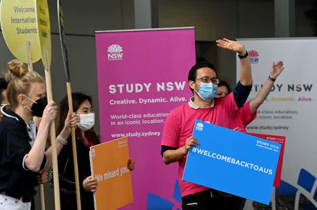 Masked people holding signs welcoming international students back to Australia
