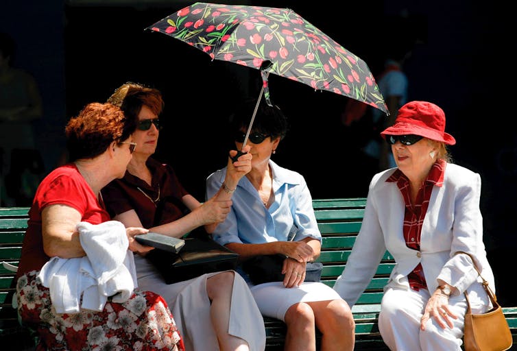 Four older women shelter from the sun under umbrella