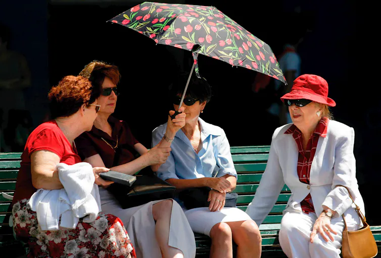 Four older women shelter from the sun under umbrella