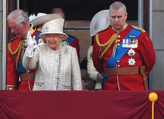 The Queen smiles and waves next to a sullen looking Prince Andrew during an official event