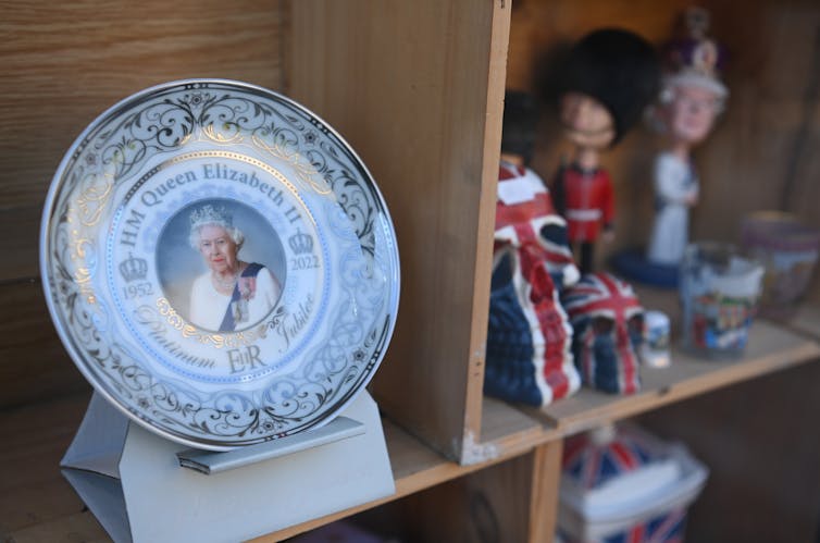 A plate with a photo of the Queen and other royal souvenirs in a shop.
