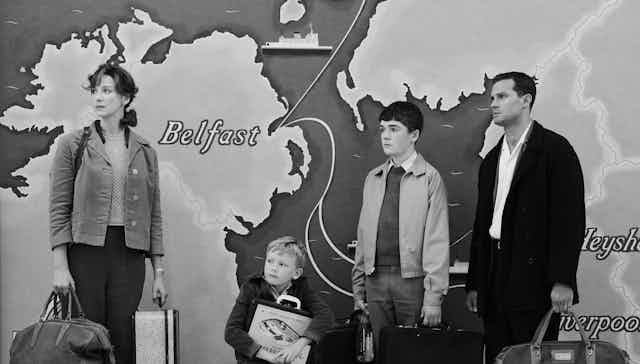A family stands with luggage in front of a map of the UK.
