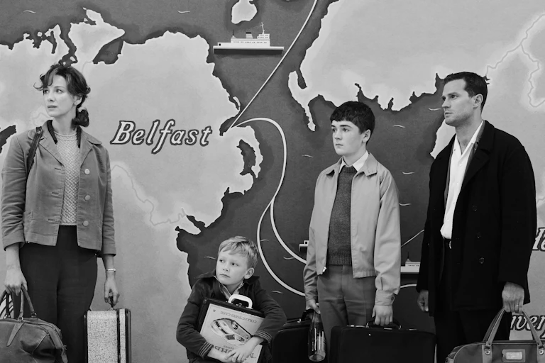 A family stands with luggage in front of a map of the UK.