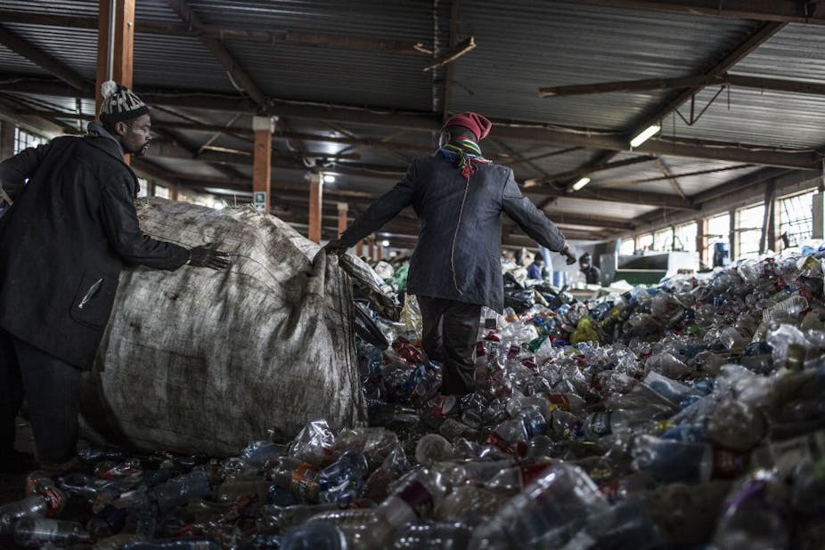 Two reclaimers emptying a bag of plastic bottles at recycling centre in Johannesburg, South Africa.