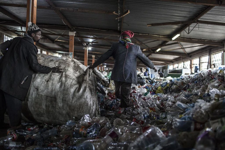 Two reclaimers emptying a bag of plastic bottles at recycling centre in Johannesburg, South Africa.