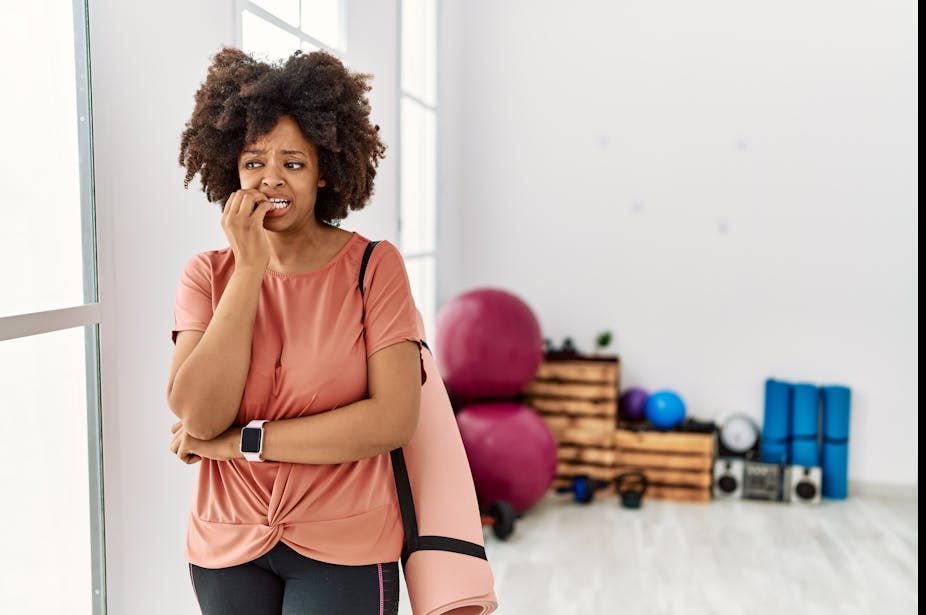 Woman in exercise clothes looks nervous about going into the gym.