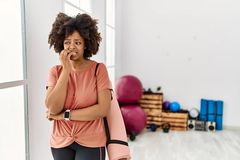 Woman in exercise clothes looks nervous about going into the gym.