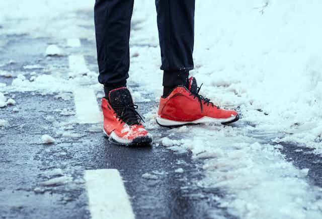 Une personne portant des chaussures de course rouges se tient sur une route enneigée.