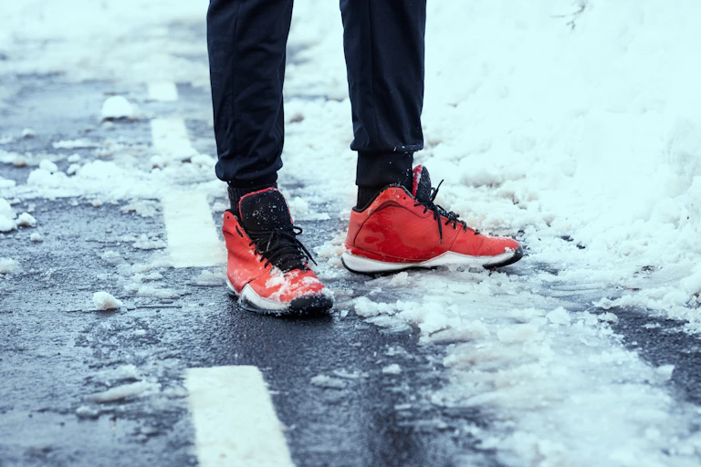 Une personne portant des chaussures de course rouges se tient sur une route enneigée.