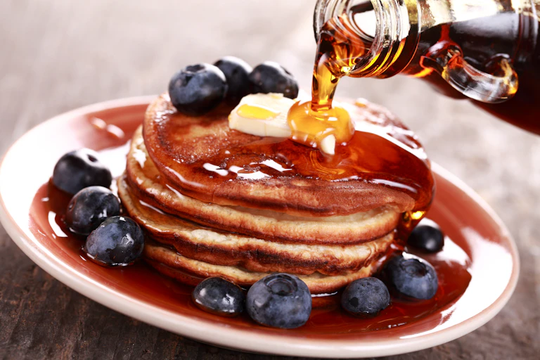 Maple syrup being poured over a stack of pancakes.