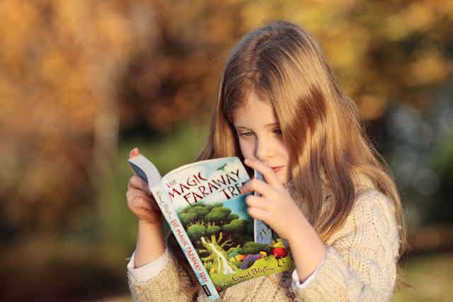 A girl reads a copy of The Magic Faraway Tree