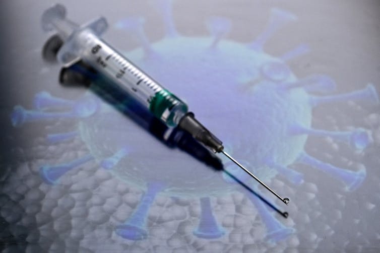 A syringe on a picture of the SARS-CoV-2 virus