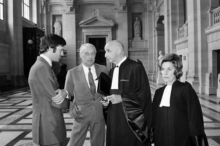 Three men holding a conversation while a woman in a black gown stands alongside.