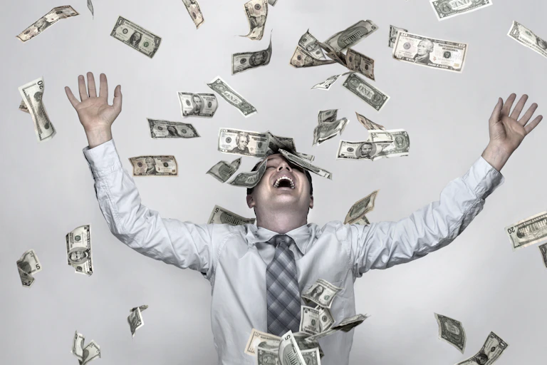 A man with his hands in the air and money falling around him.