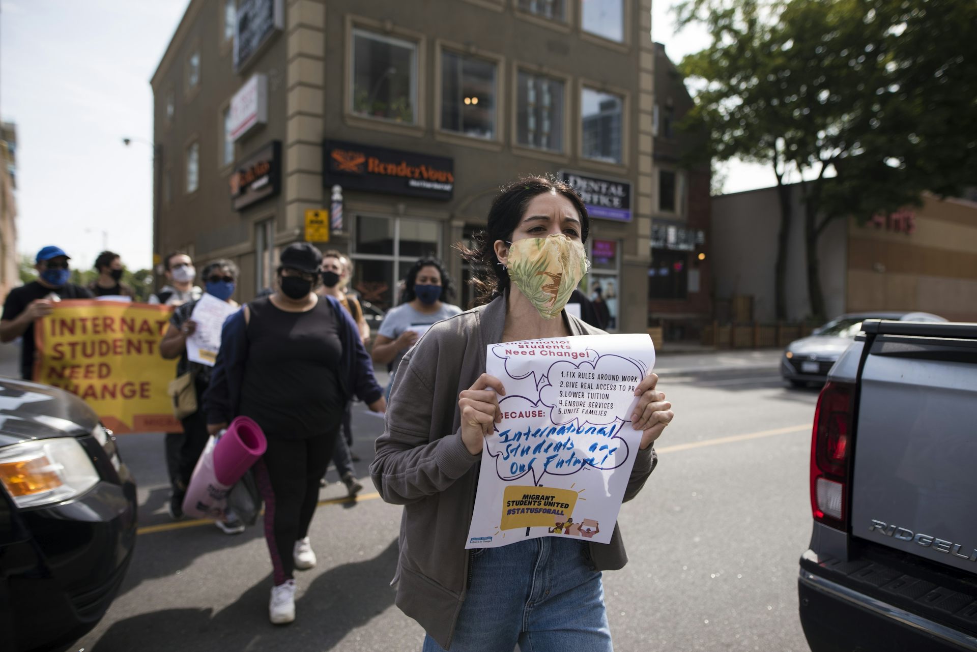 People are seen at a rally and there is a sign reading 'international students need change'