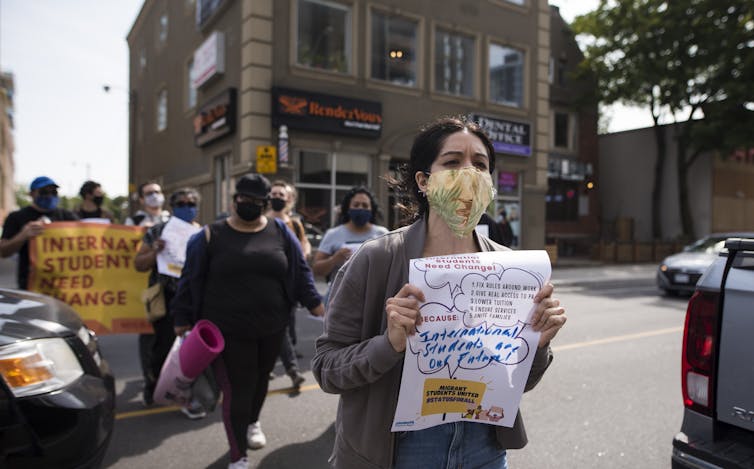 People are seen at a rally and there is a sign reading 'international students need change'