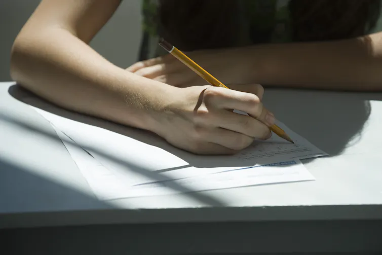 A person holding a pencil above a sheet of paper.