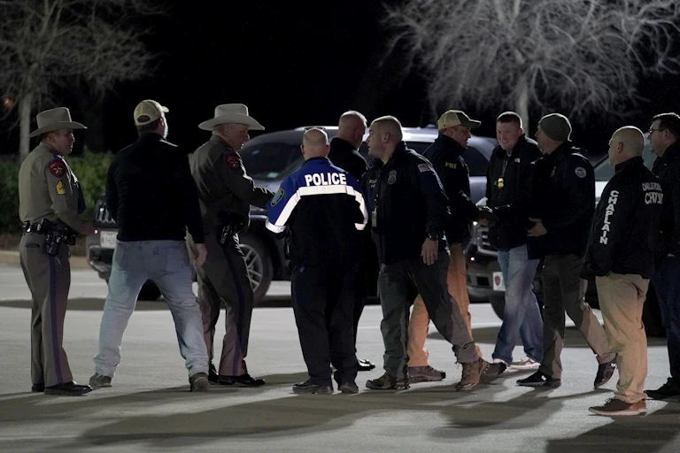 Several male law enforcement officials standing in front of a car and holding a conversation.