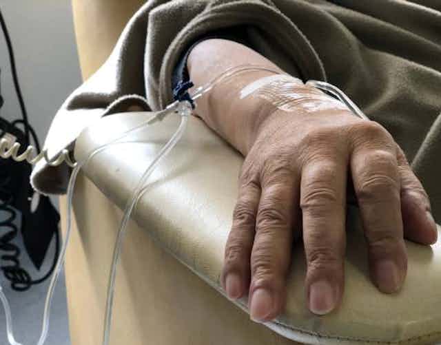 An intravenous line is taped to a hand resting on a chair's armrest.