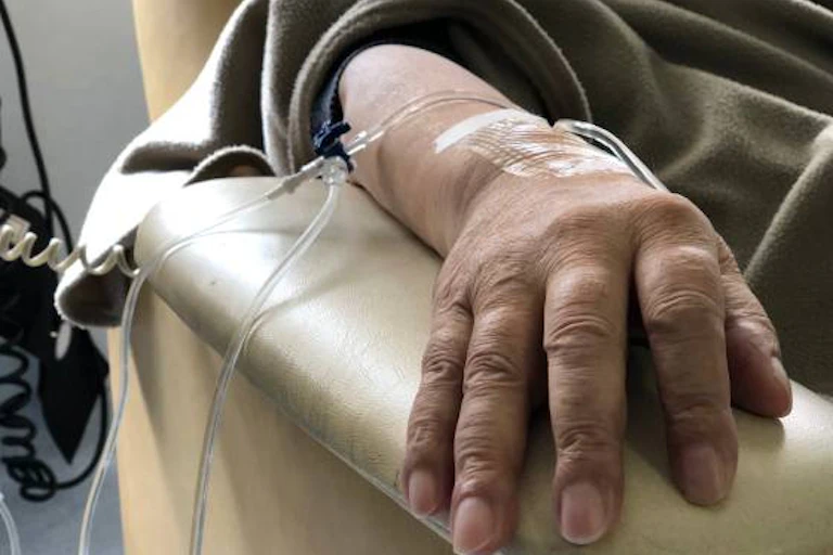 An intravenous line is taped to a hand resting on a chair's armrest.