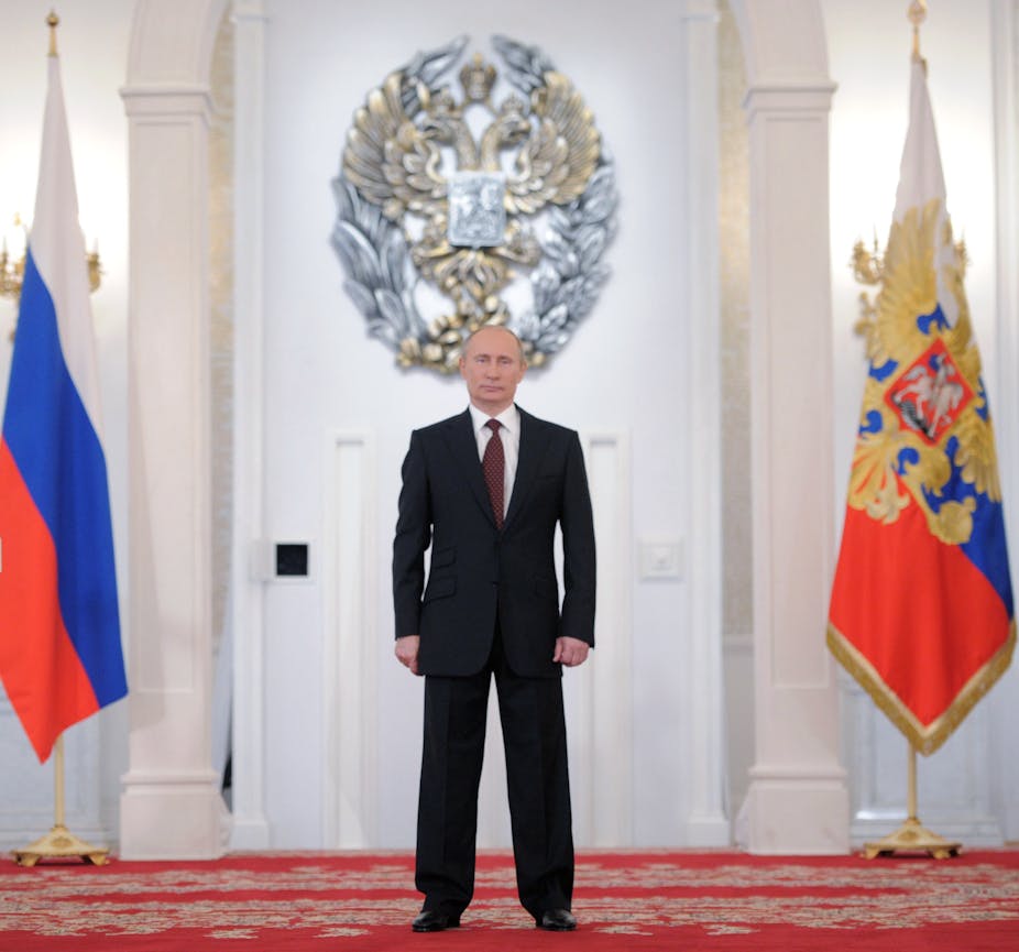 Vladimir Putin stands between two Russian flags
