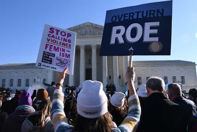 Anti-abortion protestors outside the Supreme Court hold up a banner stating, 'Overturn Roe.'