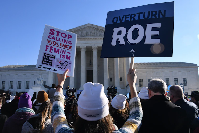 Anti-abortion protestors outside the Supreme Court hold up a banner stating, 'Overturn Roe.'