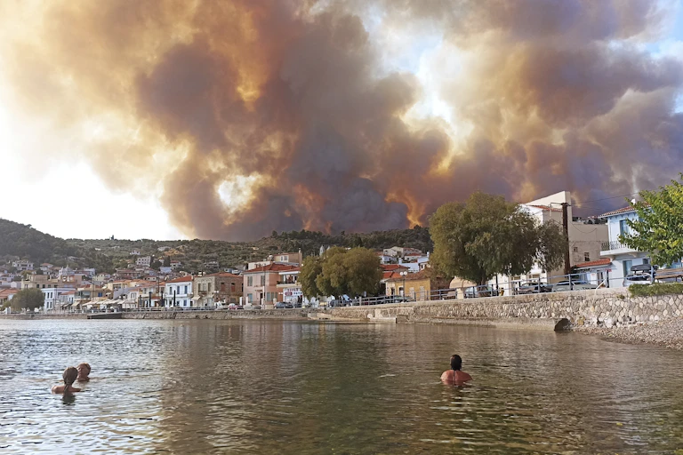 People swimming, watching smoke from a wildlife in the distance