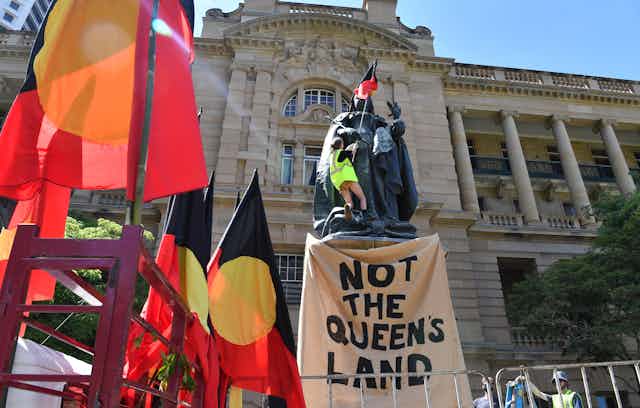 A protestor places an Aboriginal flag on a statue of Queen Victoria. 