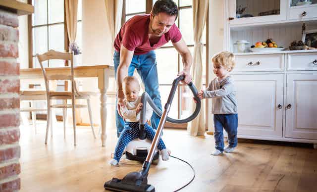 A man vacuuming while looking after two toddlers