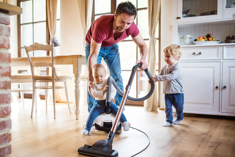 A man vacuuming while looking after two toddlers
