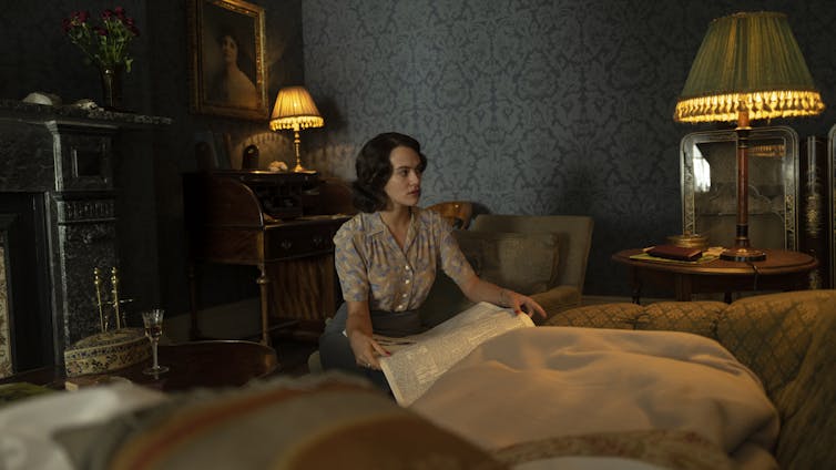 A woman kneels by a bed.