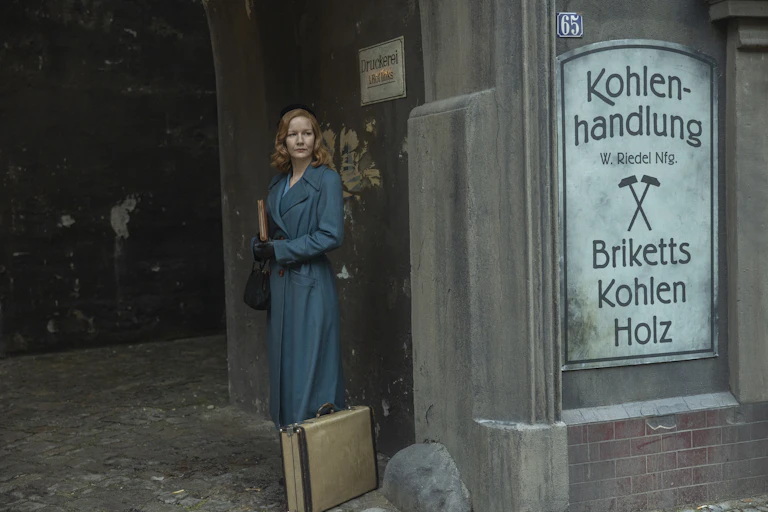 A woman in a blue coat stands in an archway.
