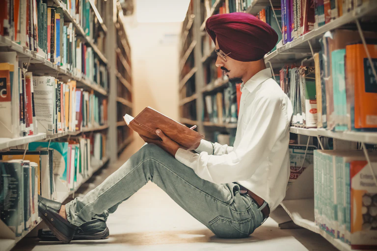 A man sits on the floor of a library engrossed in a book.