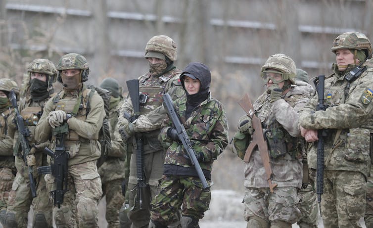 Male and female soldiers in combat gear carrying assault weapons.