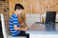 A boy with a clarinet looking at a screen.