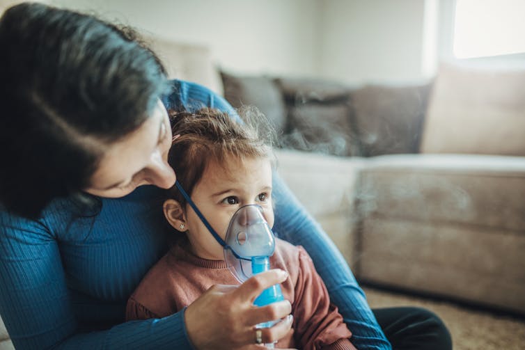 A woman holding a child wearing a nebulizer face mask to inhale medicine